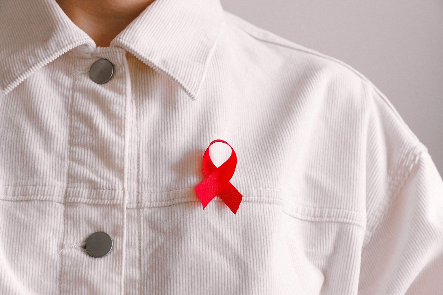 Uma pessoa com uma camisa branca veste uma fita vermelha, símbolo de solidariedade com pessoas infectadas pelo VIH e doentes com SIDA.