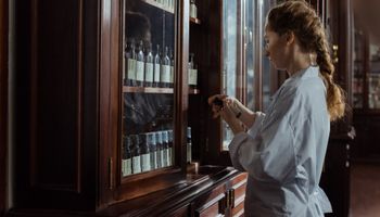 Woman opens a pharmacist's cabinet made of wood and glass and inspects a medicine.