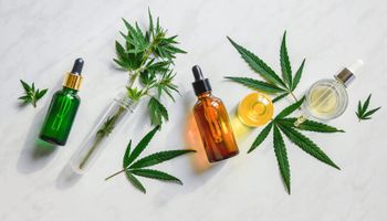 Various glass bottles with CBD oil, THC tincture and hemp leaves on marble background. Flat position, minimalism. Cosmetics CBD oil.