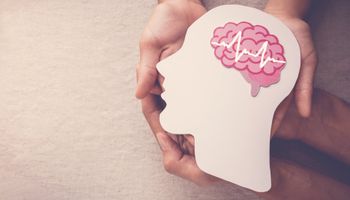 Dois pares de mãos segurando uma cabeça cortada de papel com um cérebro desenhado com uma encefalografia simbólica simbolizando a epilepsia.