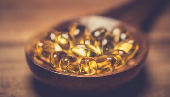 Vitamin D capsules in a wooden spoon on a wooden table.