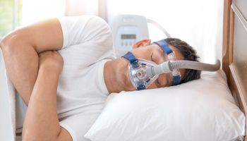 Un señor mayor lleva una máscara respiratoria mientras está tumbado de lado en la cama intentando conciliar el sueño.