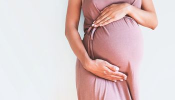 Uma mulher grávida segura a sua barriga. O fundo é branco.