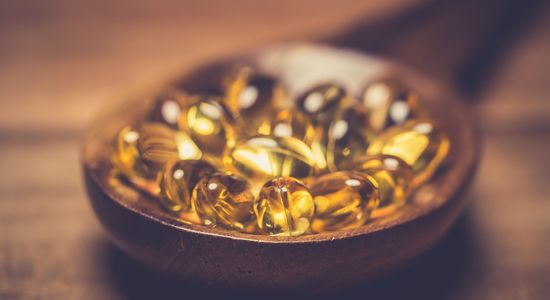 Des capsules de vitamine D dans une cuillère en bois sur une table en bois.