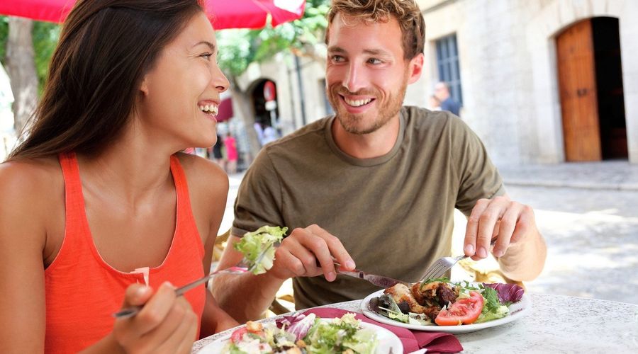 Twee mensen eten in een restaurant en glimlachen naar elkaar.