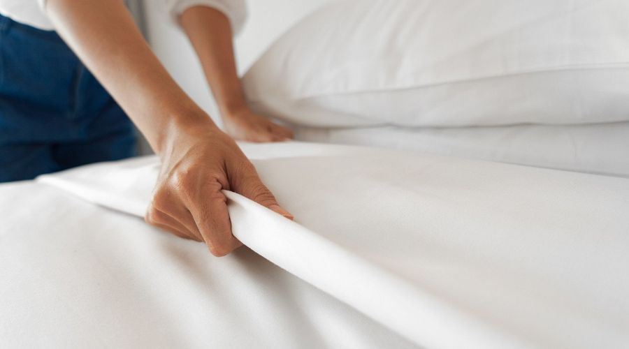 Una persona cubre una cama. Sólo se ven los brazos y parte de la cama.