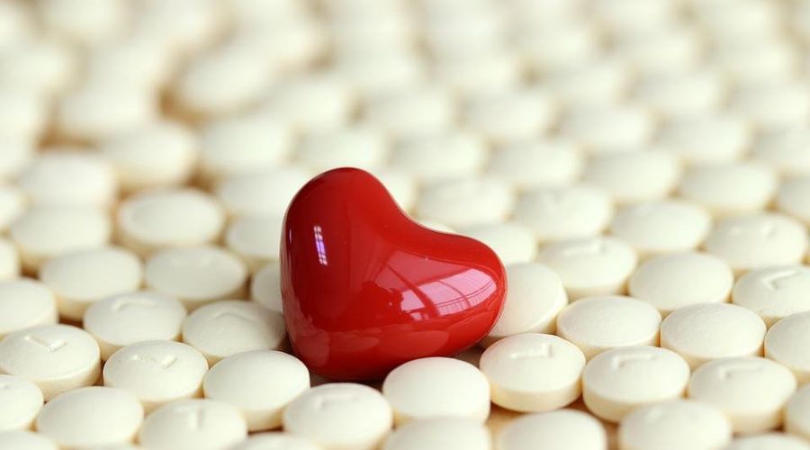 Close-up van een keramische hartvorm in rood, omgeven door tabletten in de kleur beige.