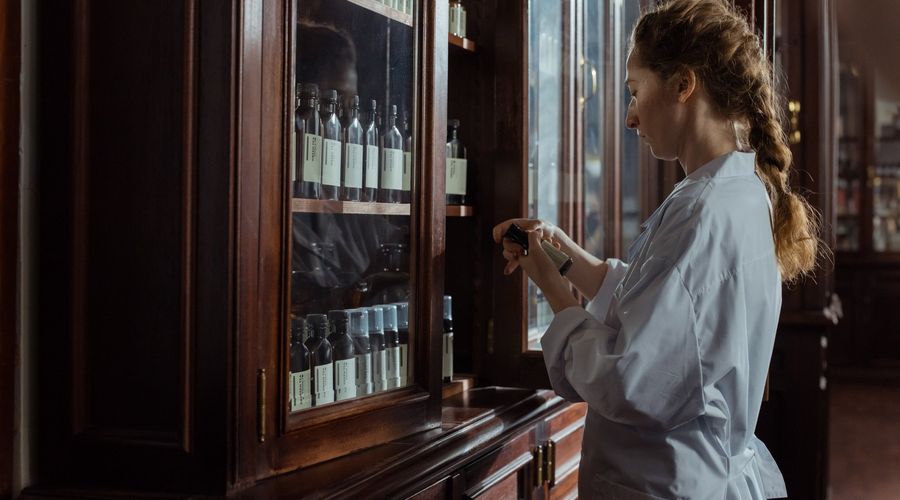 Woman opens a pharmacist's cabinet made of wood and glass and inspects a medicine.