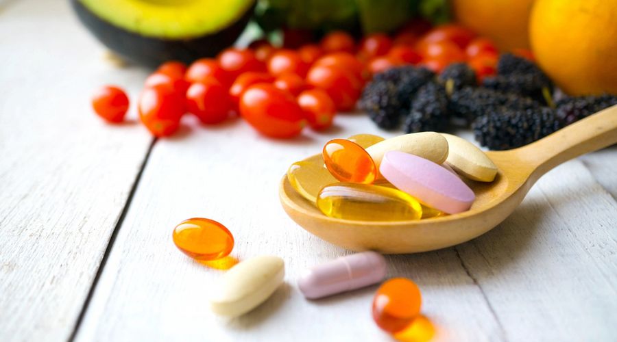 Pilules et gélules dans une cuillère en bois avec des fruits frais.Multivitamines et complément du concept de fruits.