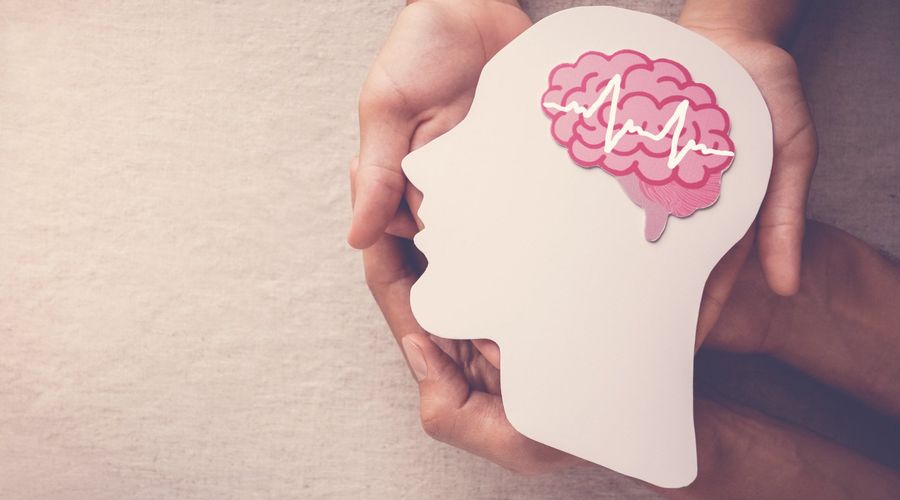 Deux paires de mains tenant une tête découpée dans du papier avec un cerveau dessiné avec une encéphalographie symbolique pour symboliser l'épilepsie.