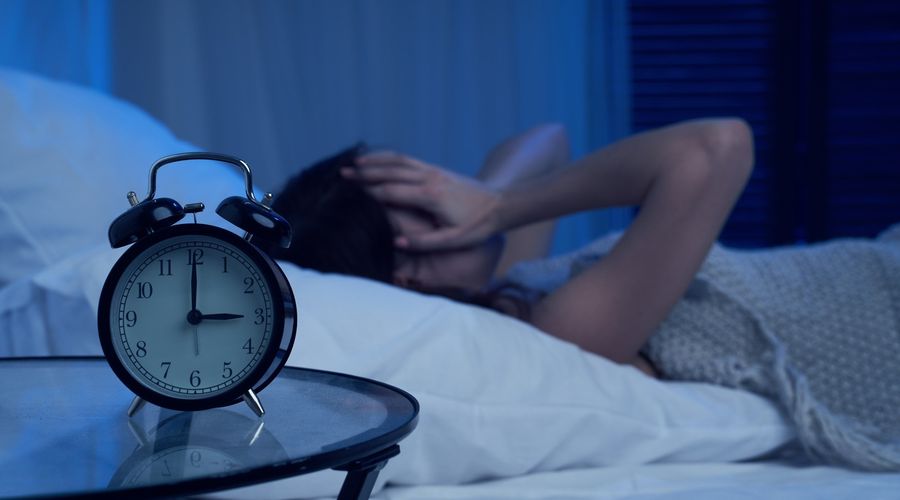 Donna infelice con insonnia sdraiata sul letto accanto alla sveglia di notte