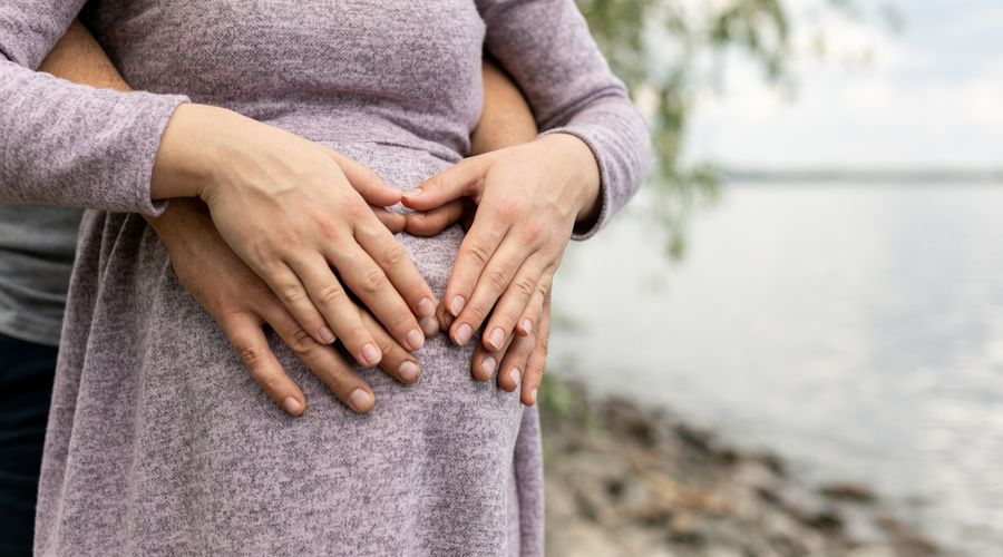 Paar handen die zwangere jonge vrouwenbuik houden