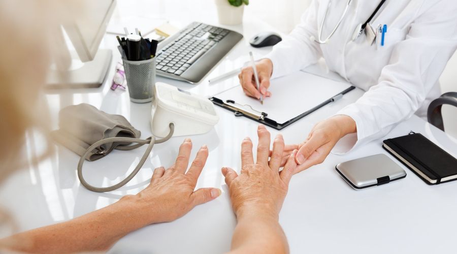 Examen médico con una anciana mostrando sus manos al médico.
