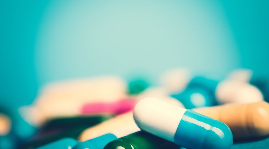 Arzneimittel-grüne und gelbe Tabletten oder Kapseln auf blauem Hintergrund mit Kopienraum.Verschreibung von Arzneimitteln zur Behandlung. Arzneimittel zur Heilung in Behältnissen für die Gesundheit. Antibiotika