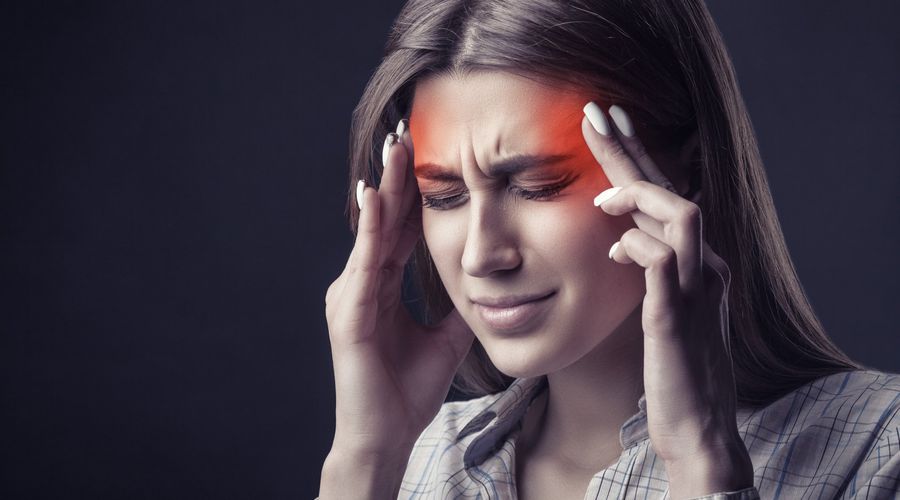 Junge Frau leidet unter Kopfschmerzen auf dunklem Hintergrund. Studioaufnahme