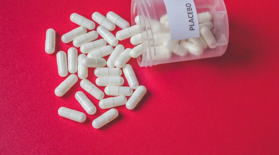 Pilules ou capsules placebo blanches s'écoulant d'une bouteille sur fond rouge, effet placebo, concept de randomisation ou de traitement, vue d'époque.