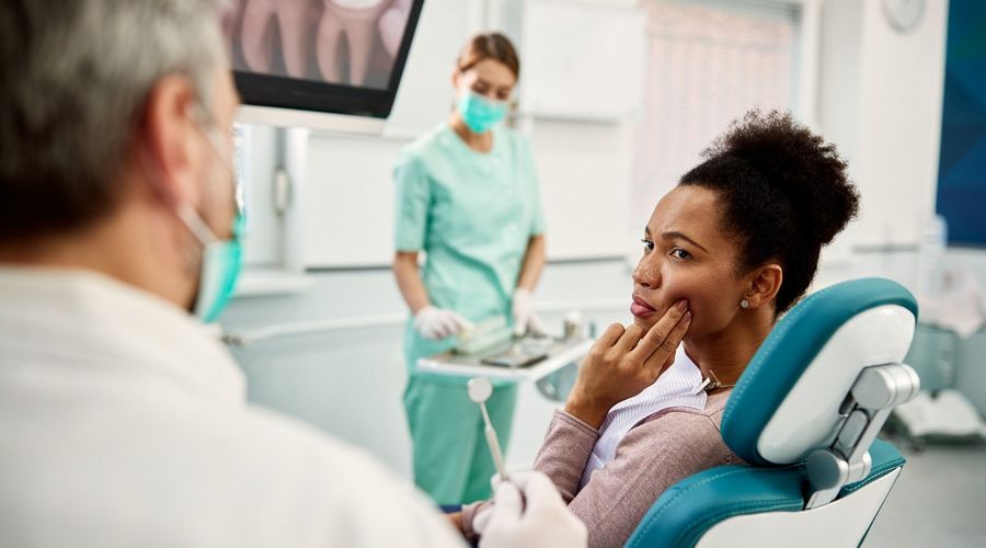 Eine Frau zeigt einem Zahnarzt im Behandlungsraum die Stelle im Mundbereich, wo Sie Zahnschmerzen hat.