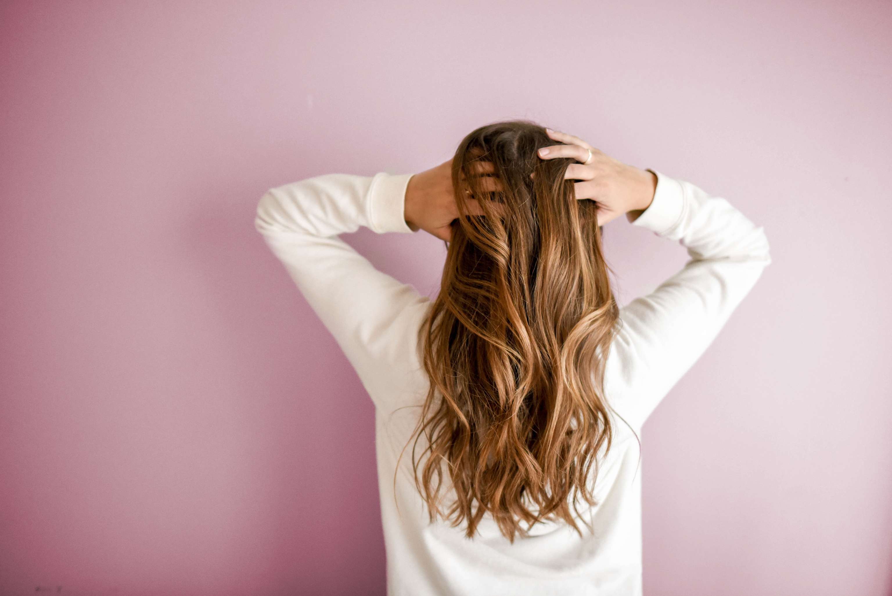 Une femme en chemise blanche se prend les cheveux dans les mains et se tient dos à la caméra.