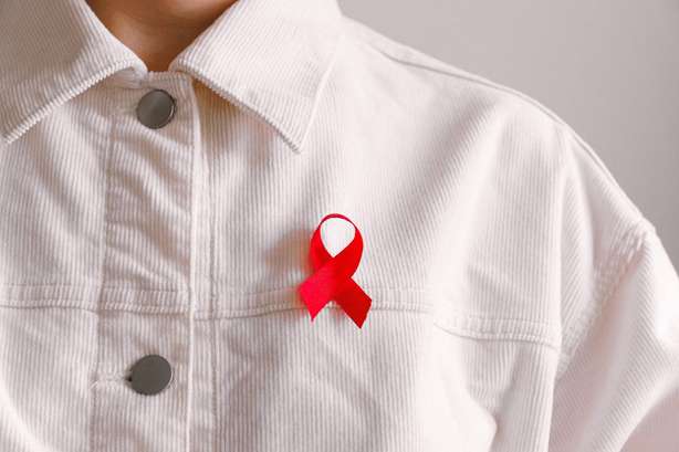 Ein Mensch im weißen Hemd trägt eine Rote Schleife, ein Symbol der Solidarität mit HIV-Infizierten und AIDS-Kranken.