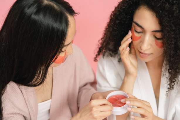 Zwei Frauen tragen eine rote Creme unter die Augen auf.