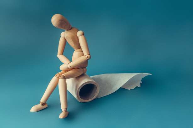 Eine hölzerne Figur sitzt auf einer Rolle Toilettenpapier. Eine hölzerne Figur sitzt auf einer Rolle Toilettenpapier. Konzept des Problems mit Verdauung.