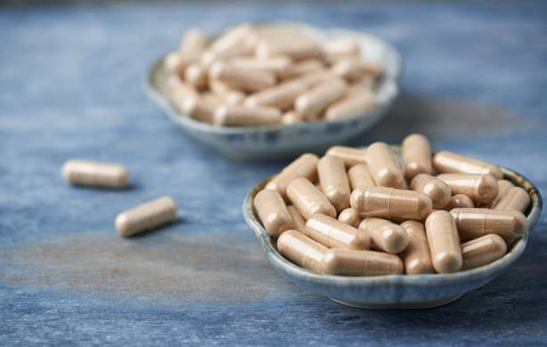Eine SchĂĽssel, die mit Kapseln gefĂĽllt ist. Ashwagandha (Withania somnifera) and Korean Ginseng capsules. Concept for a healthy dietary supplementation. Rustic wooden background. Copy space.