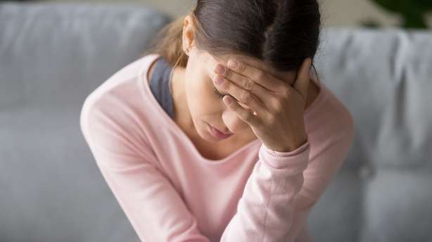 Young tired unhealthy mixed race woman sitting on sofa in living room at home with eyes closed, holding head with hand, suffering from severe sudden headache or migraine, whirling pain.