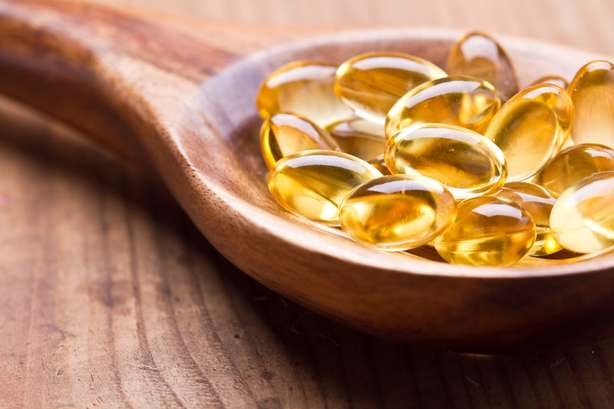 Omega-3-Gel-Kapseln in einem Holzlöffel. Cod-Leberöl-Omega-3-Gel-Kapseln einzeln auf Holzhintergrund