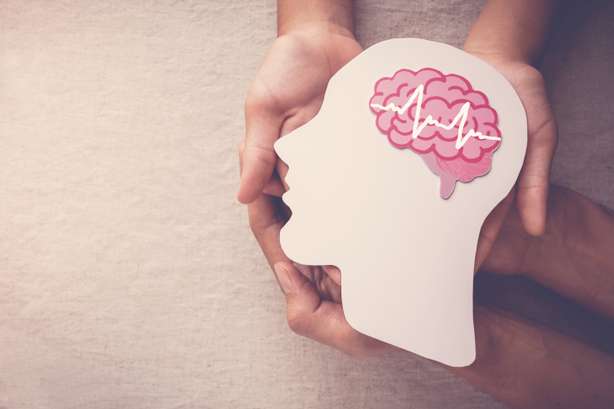 Deux paires de mains tenant une tête découpée dans du papier avec un cerveau dessiné avec une encéphalographie symbolique pour symboliser l'épilepsie.