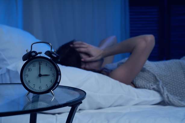 Eine an Schlaflosigkeit leidende Frau liegt im Bett neben einem Wecker. Unglückliche Frau mit Schlaflosigkeit, die am Bett neben dem Wecker in der Nacht liegt