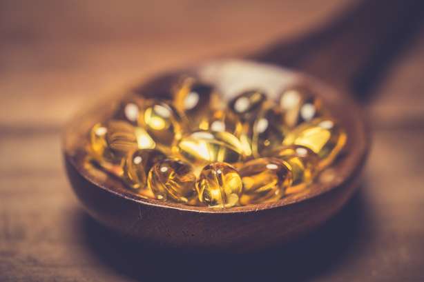 Cápsulas de vitamina D em uma colher de madeira sobre uma mesa de madeira.
