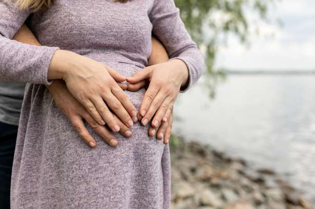 Paar Händen, die einen Bauch von schwangeren jungen Frauen halten Ein Paar haltet den Bauch der schwangeren Frau.