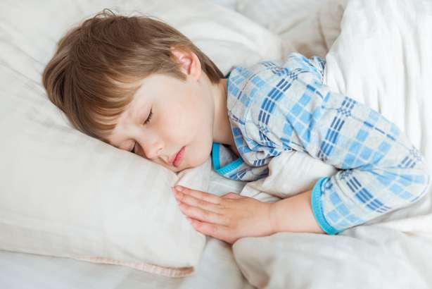 Schöner kleiner Junge, der im Bett schläft Kleiner Junge liegt im Bett mit geschlossenen Augen.