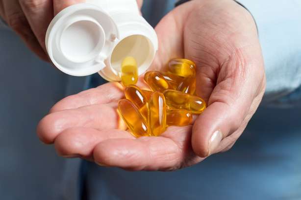 Die weibliche Hand hält gelbe Medikamentenkapseln von Omega 3, Griechen aus einer weißen Flasche in Palme das Fischöl, gesunde Beipackzettel.
