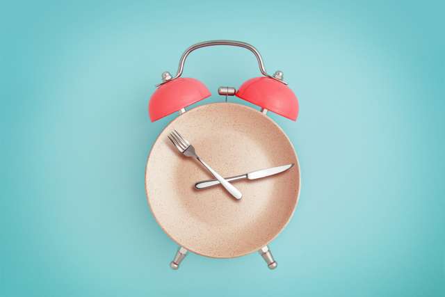 Sveglia e piatto con posate. concetto di digiuno intermittente, pranzo, dieta e perdita di peso
