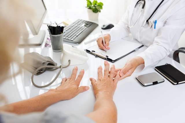 Nahaufnahme einer ärztlichen Untersuchung.Frau im mittleren Alter mit Arthritis, die einer weiblichen Ärztin die Hände zeigt.