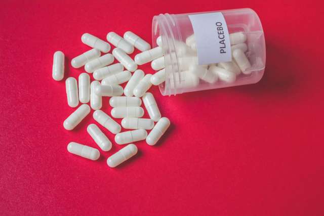 Witte placebopillen of capsules die uit een fles op rode achtergrond, placebo-effect, randomisatie of behandelingsconcept, uitstekende mening morsen