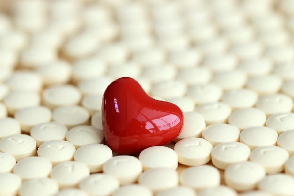 Close-up van een keramische hartvorm in rood, omgeven door tabletten in de kleur beige.