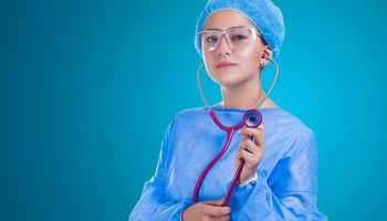 Primo piano di una donna in camice ospedaliero con in mano uno stetoscopio.