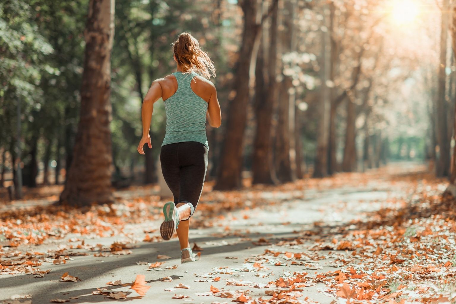 Mujer corriendo por un camino forestal - Una buena forma física contribuye a mejorar la salud de varias maneras.