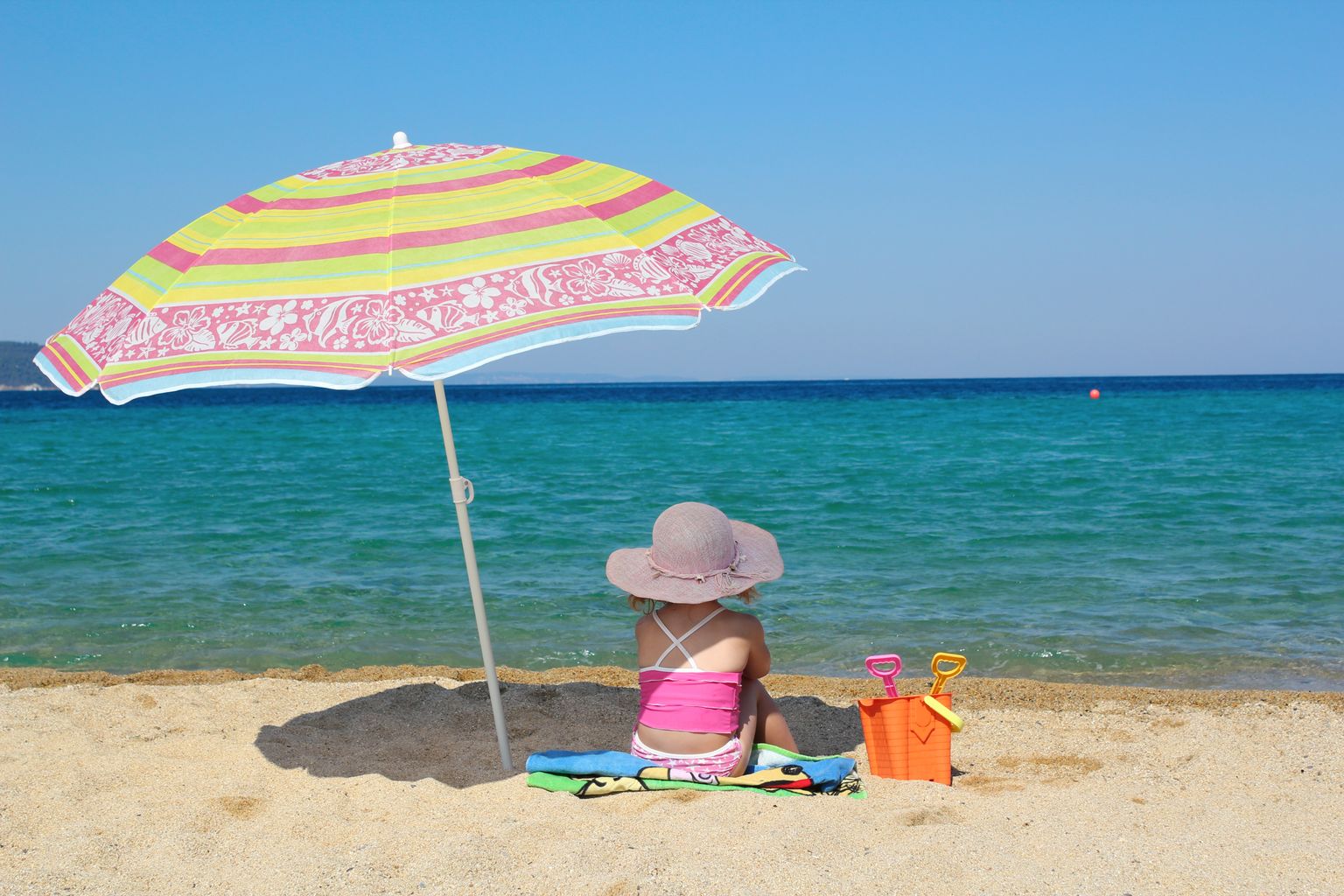 Little girl sitting on beach under umbrella