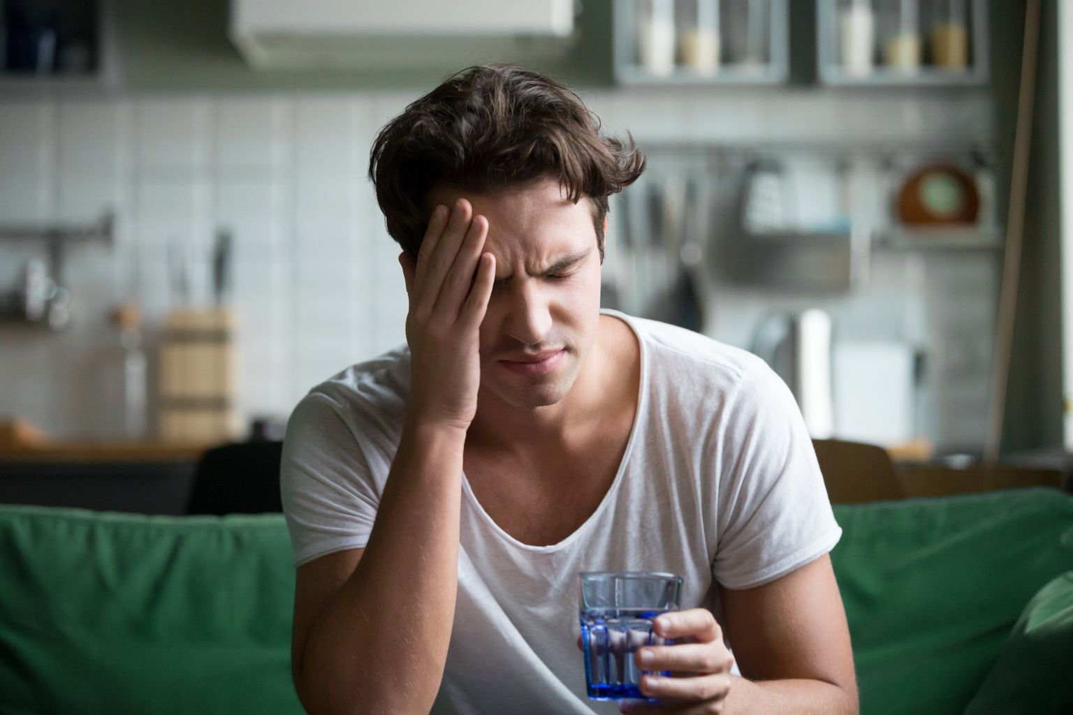 Aufnahme von jungem Mann mit KOpfschmerzen und einem Glas Wasser in der Hand