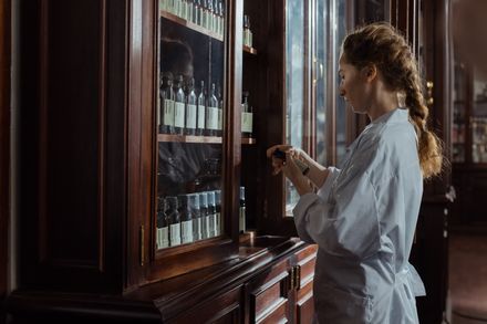 Frau öffnet einen Apotheker-Schrank aus Holz und Glas und inspiziert ein Arzneimittel.