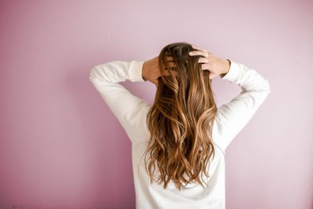 A woman with a white shirt grabs her hair and stands with her back facing the camera.