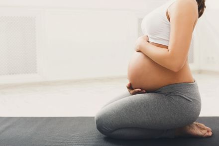 Mujer embarazada irreconocible practicando yoga en la postura del héroe, acariciando su vientre. La joven expectativa feliz se relaja, piensa en su bebé y en su futuro
