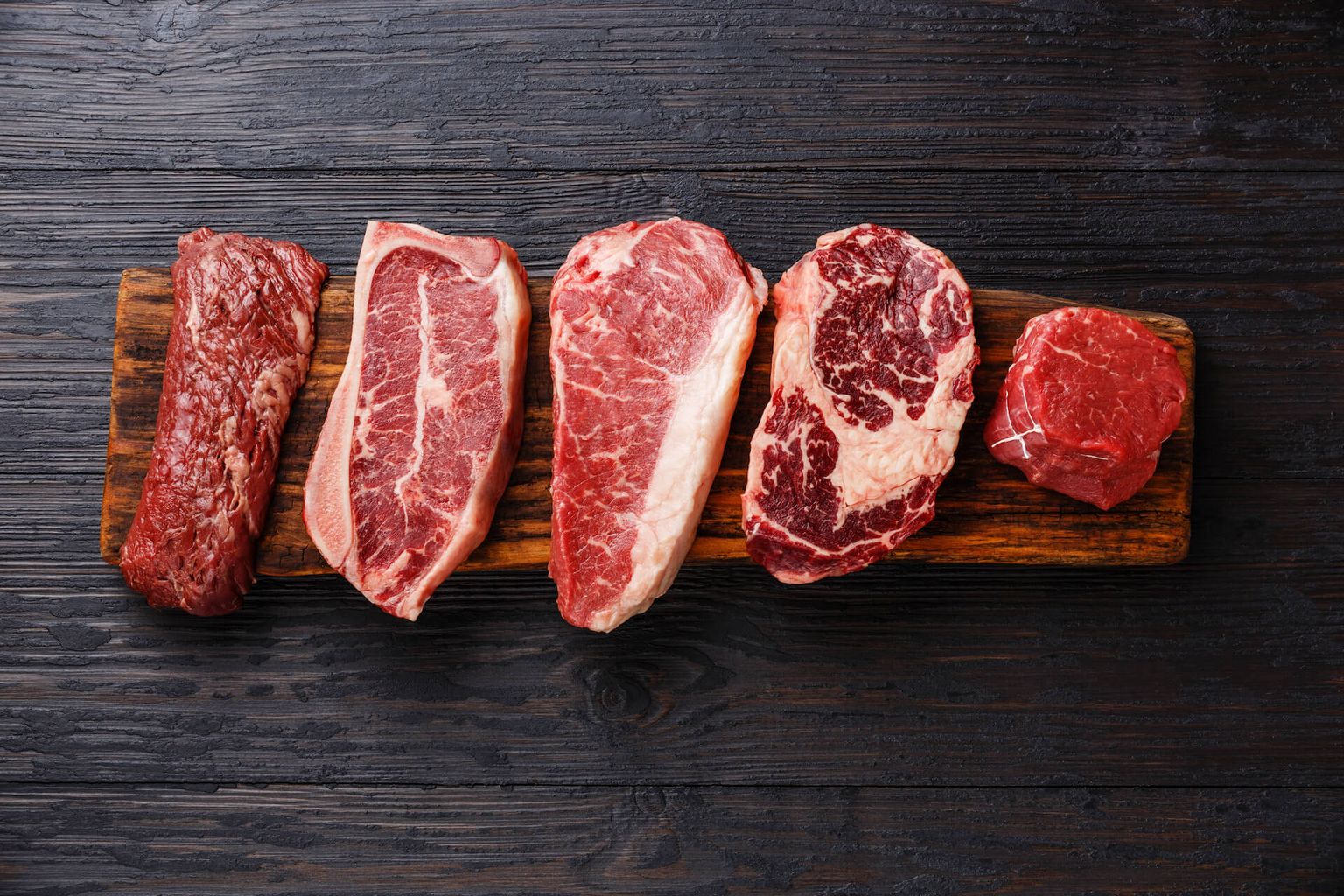 Variety of Raw Black Angus Prime Fleisch Steaks Machete, Blade auf Knochen, Striploin, Rib eye, Tenderloin Filet Mignon auf Holzbrett Kopienraum