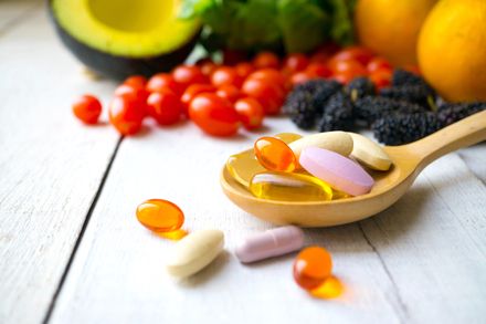 Pillole e capsule in un cucchiaio di legno con frutta fresca. Multivitamine e integratori dal concetto di frutta.