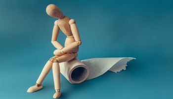 A wooden figure sits on a roll of toilet paper. Concept of the problem with digestion.