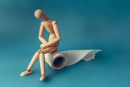 Een houten figuurtje zit op een rol toiletpapier. Concept van het probleem met de spijsvertering.