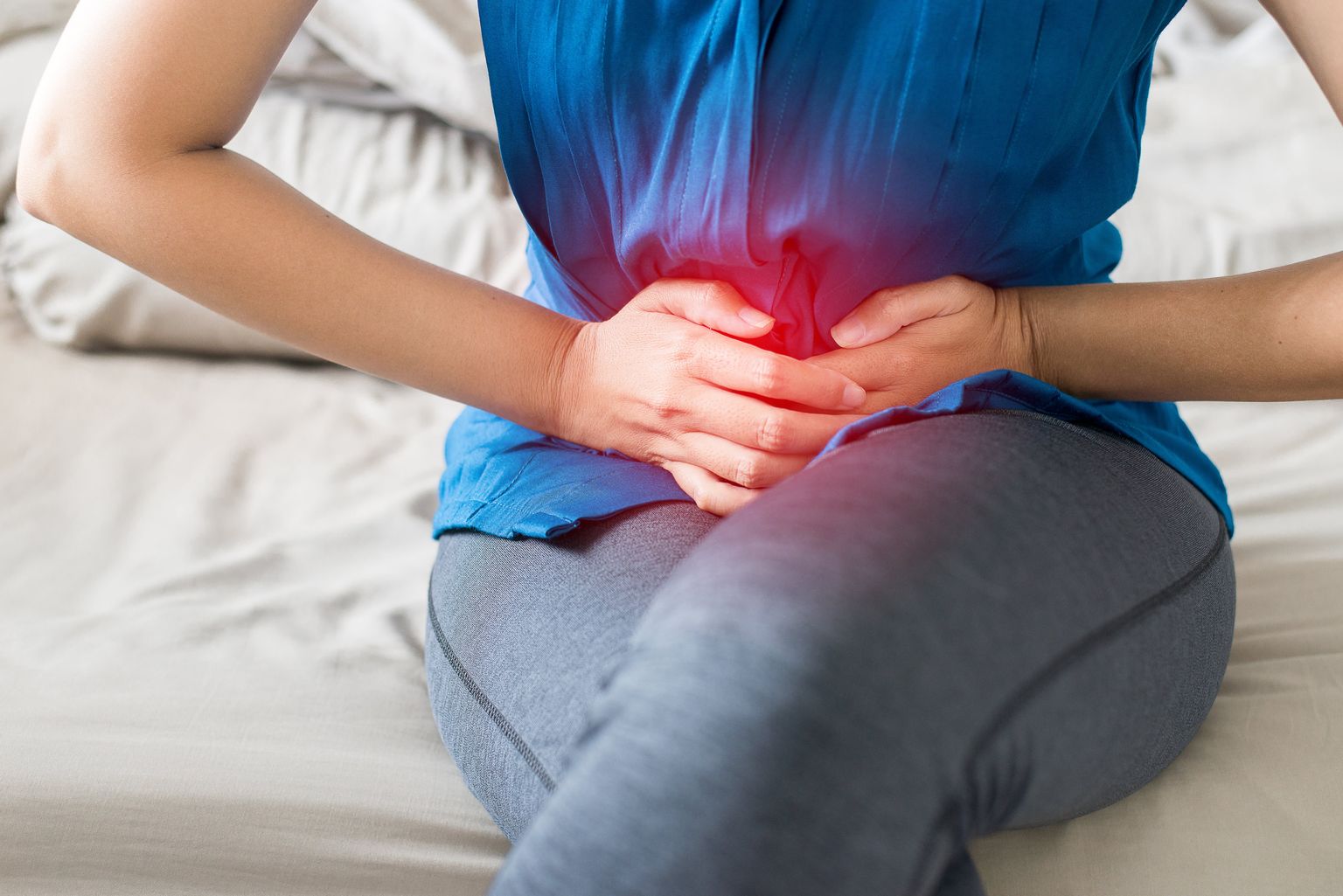 Una mujer se sienta y se lleva las manos al bajo vientre para representar simbólicamente el dolor menstrual.